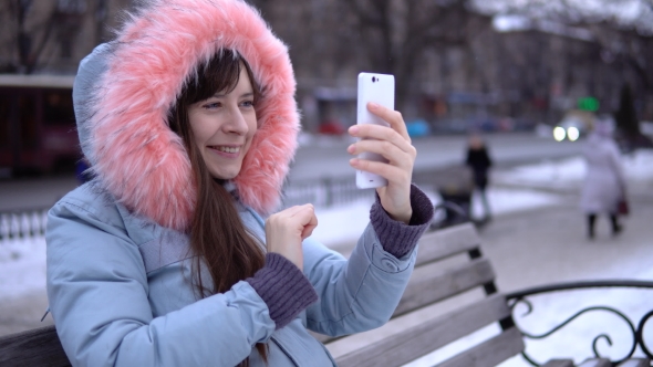 Young Woman in a Gray Warm Jacket Uses a Phone in the Street in the Winter