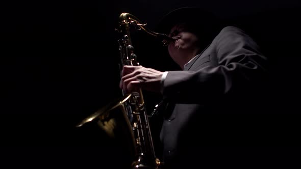 Male musician in a formal suit enjoys playing the saxophone in dark of studio.
