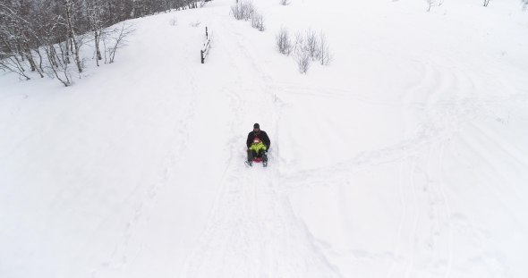 Winter Aerial  Follow Father Riding Red Bobsled on Snowy Downhill with Child.Dad, Son or Daughter