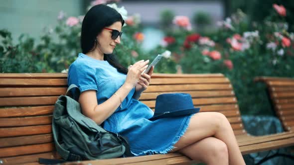 Woman Tourist with Mobile Phone is Sitting in the Park in Warm Spring Day