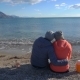 Back View of Romantic Couple Sitting on the Beach and Look at the Sea - VideoHive Item for Sale