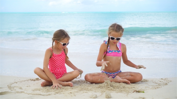 Adorable Little Girls Playing with Sand on the Beach. Kids Sitting in Shallow Water and Making a