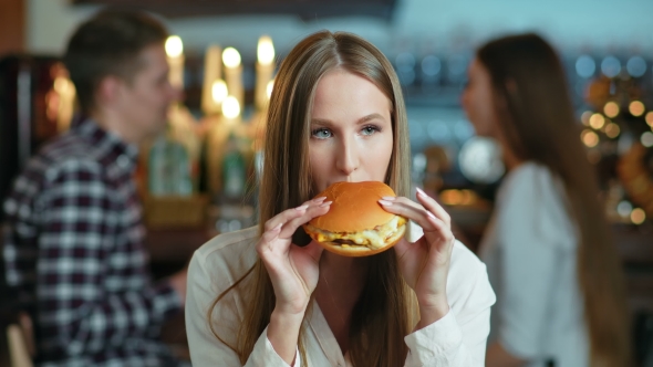 Young Happy Woman Eating Tasty Fast Food Burger in Cafe