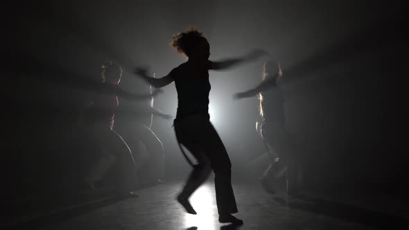 Young People Practicing Capoeira in Darkness Against Spotlight in Studio