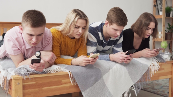 Group of Internet-addicted Teenegers Lying on Bed and Looking at Smartphones