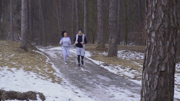 Young Woman with Man Runs Along Slippery Winter Road in the Forest