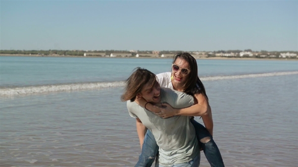 Young Funny Couple in Sunglasses Piggybacking on the Beach. Friends Together Having Fun. Sea Is 