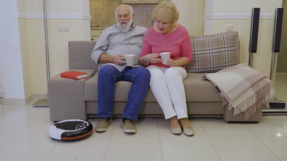 Old People Relax at Sofa During Vacuum Cleaner Clean the Floor in Living Room