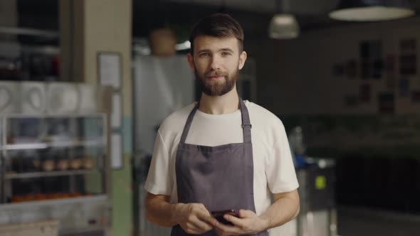 Bearded Waiter Using Cell Phone for Work at Cafe