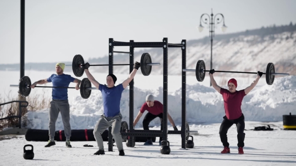 Four Powerlifters Is Training in a Winter Day Outdoors, Lifting Heavy Rods, Standing on a Snowy