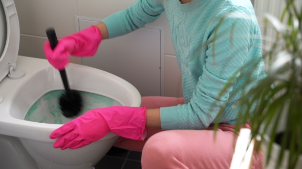 Woman with a Rubber Glove Cleans a Toilet Bowl