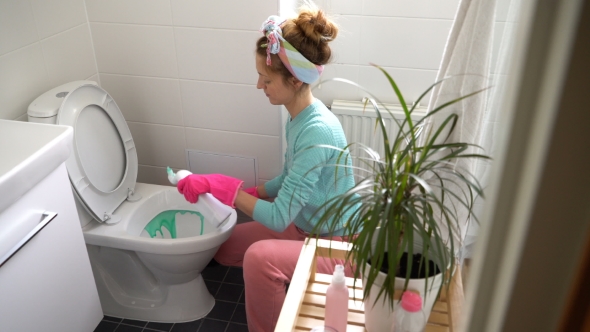 Woman with a Rubber Glove Cleans a Toilet Bowl