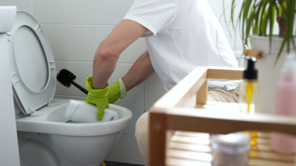Man with a Rubber Glove Cleans a Toilet Bowl
