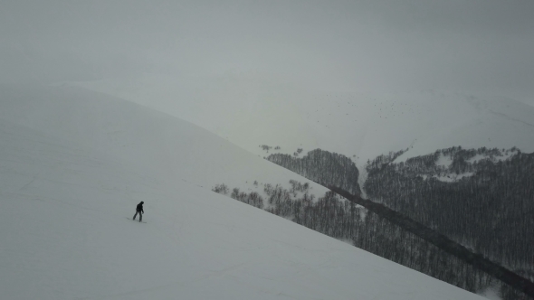 Snowboarder Descending By a Mountain Ridge. Birds Eye View Above White Powder Snow
