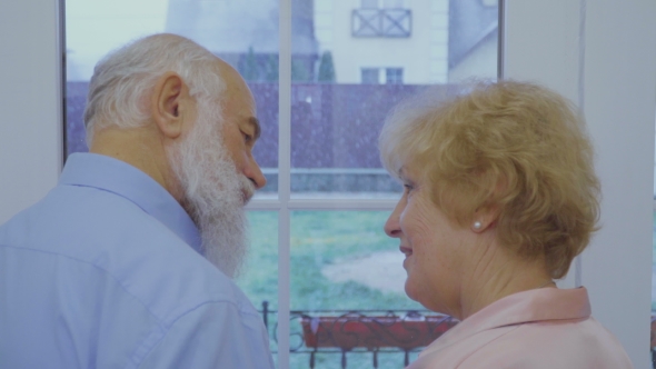 Married Senior Couple Enjoys Falling Snow in the Window