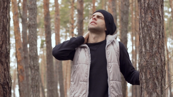 Young Man Suffers From Neck Pain Stands Near Tree in the Forest