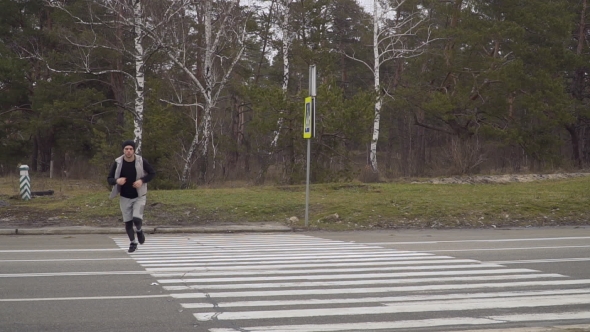 Young Sportsman Crosses the Road, Stops, Checks the Time and Continue Running