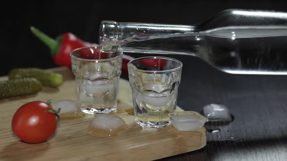 Pour Vodka From a Bottle Into Shot Glasses with Ice Cubes