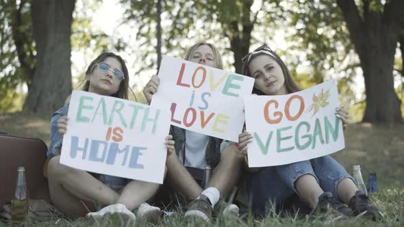 Three Young Hippies Showing Posters Earth Is Home Love Is Love Go Vegan Looking Camera