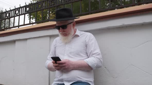 Old Man with Albinism Browsing on the Internet While Sitting Next To His House