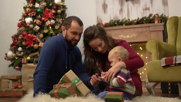Cute Fun Family Celebrating Christmas Together Mother, Father and Little Baby Sitting on the Floor
