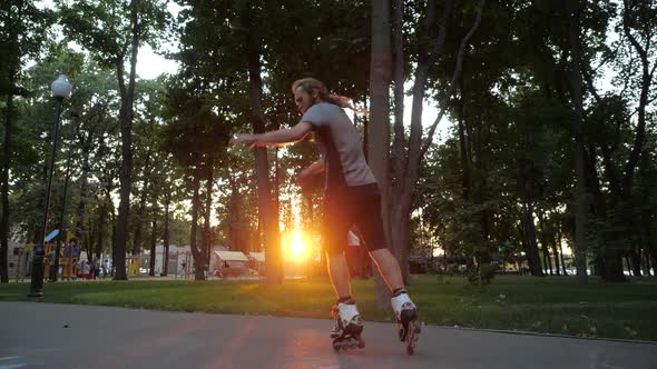 Young Long-haired Bearded Man Roller Skater Is Dancing in a Nice Evening in a City Park. Freestyle