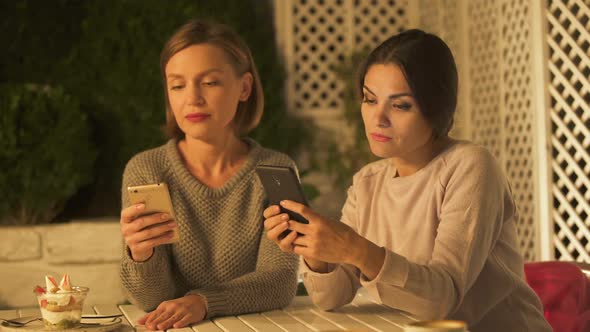 Female Friends Scrolling Phones Trying to Find Photos, Discussing Shopping