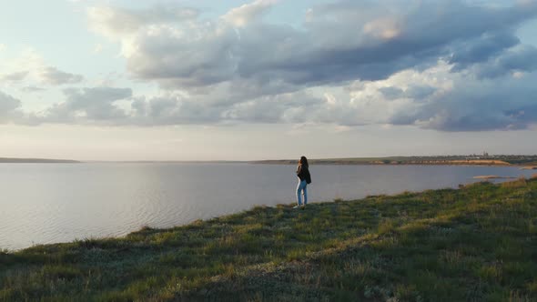 Tracking Aerial Shot of Young Woman Enjoying Sunset in Field Near the Cliff During Beatiful Sunset