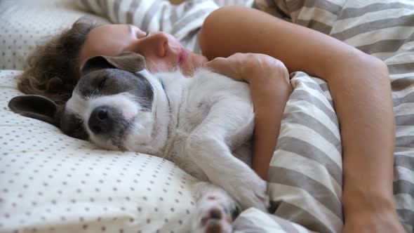 Girl And Her Pet Dog Hugging In The Bed.