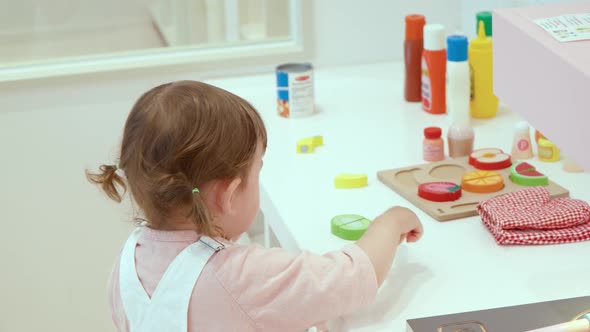 Little Girl Slicing Wooden Vegetable With A Wooden Knife At Kid's Cafe - Kitchen Set Cooking Toys. -