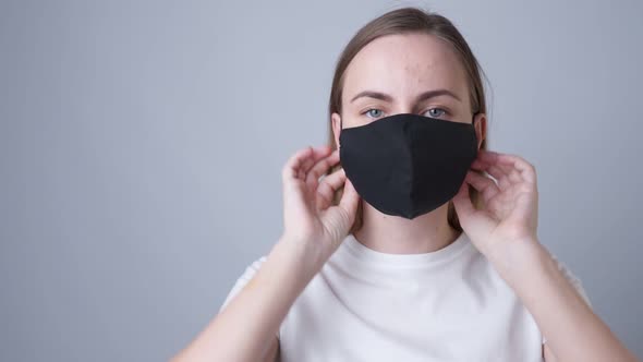 Woman Puts a Black Medical Mask on Her Face on a Gray Background