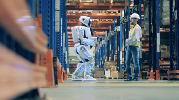 Engineer with a Laptop Is Managing a Human-like Robot in the Warehouse