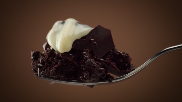 Piece of Chocolate Cake on Fork with Slowly Moving Drops of White Cream on It