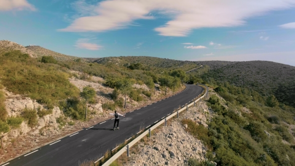 Hipster Man Rides on Skateboard on Mountain Road