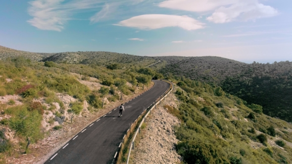 Hipster Man Rides on Skateboard on Mountain Road