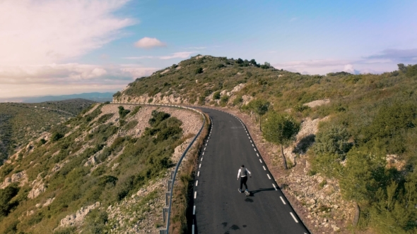 Hipster Man Rides on Skateboard on Mountain Road