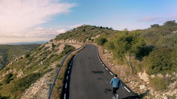 Hipster Man Rides on Skateboard on Mountain Road