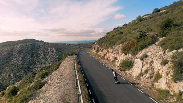 Hipster Man Rides on Skateboard on Mountain Road