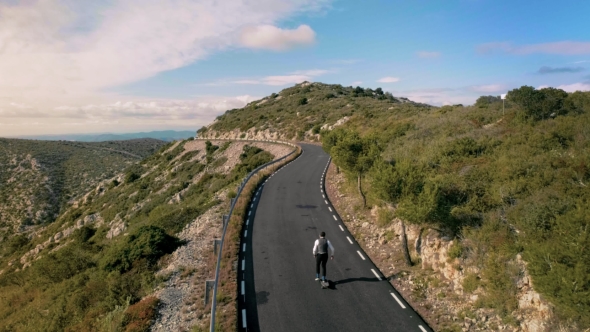 Hipster Man Rides on Skateboard on Mountain Road