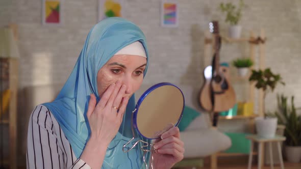 Muslim Woman in a Hijab Looks in the Mirror at Her Scar From a Burn on Her Face