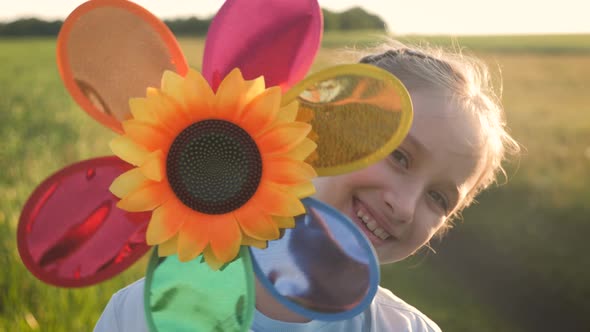 Happy Girl Holding Wind Toy in Green Field, Rejoicing Life. Cheerful Child in the Meadow with Wind