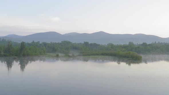 Aerial gliding over lake shoreline tranquil morning fog mountains in distance