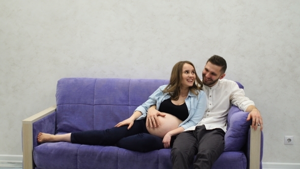 A Married Couple Is Sitting at Home on the Couch Waiting for the Birth of a Child The Man Stroked
