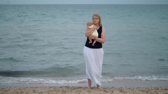 Mother with Lost Look Holding Baby Being Alone at the Beach Near Sea