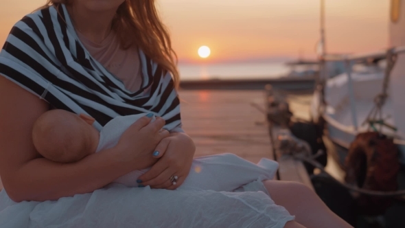Mother Nursing and Caressing Baby Sitting on the Pier at Sunset
