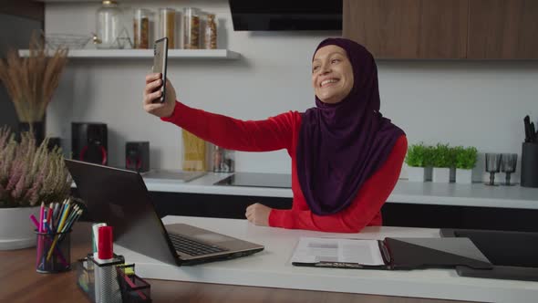 Joyful Attractive Middle Eastern Female in Hijab Posing for Selfie Shot on Cellphone Indoors