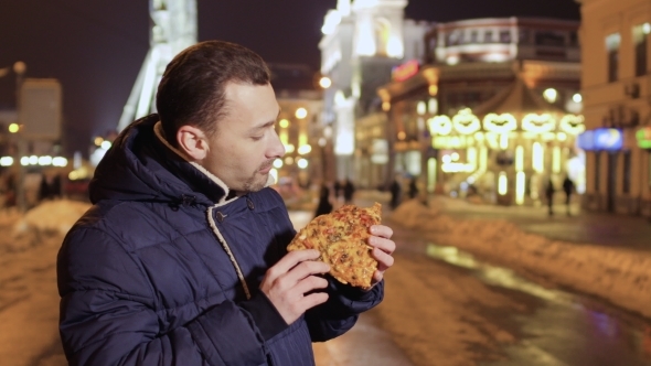 Young Man Enjoys Street Food and Eats Pizza at Night City Background