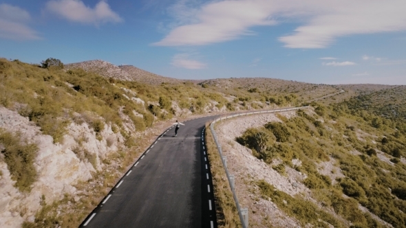 Hipster Man Rides on Skateboard on Mountain Road