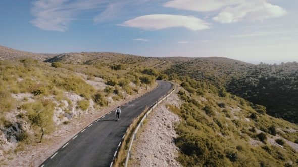 Hipster Man Rides on Skateboard on Mountain Road