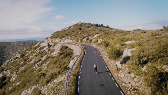 Hipster Man Rides on Skateboard on Mountain Road